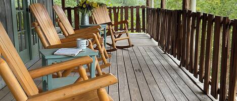 Een houten terras met buitenmeubilair, waaronder stoelen en tafels, en een uitzicht op groen in de verte.