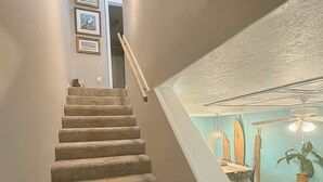 Una scala conduce a una stanza con vista sull'oceano, quadri appesi al muro e una ventola a soffitto.