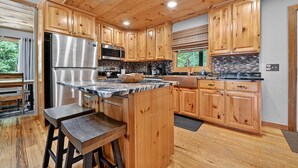 A modern kitchen with wooden cabinets, stainless steel appliances, and a marble countertop. - Bigfoot's Solitude | Game Room | Outdoor Firepit | Grill (Morganton)