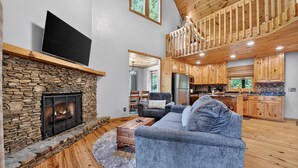 A spacious living room with a stone fireplace, a flat-screen TV, and a cozy seating area. - Bigfoot's Solitude | Game Room | Outdoor Firepit | Grill (Morganton)