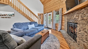 A cozy living room with a wooden staircase, a stone fireplace, and a blue sofa. - Bigfoot's Solitude | Game Room | Outdoor Firepit | Grill (Morganton)