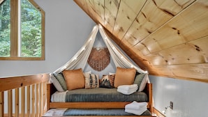 A cozy loft bedroom with a wooden ceiling, a large window, and a bed with multiple pillows and a blanket. - Bigfoot's Solitude | Game Room | Outdoor Firepit | Grill (Morganton)