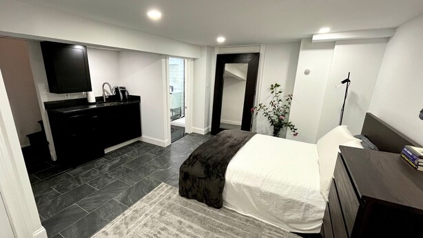 A modern bedroom with a large bed, a dark wooden dresser, a flat-screen TV, and a small desk area. - Modern Studio: minutes to NYC/Views, 4 miles from World Cup - MetLife Stadium (Weehawken Township)