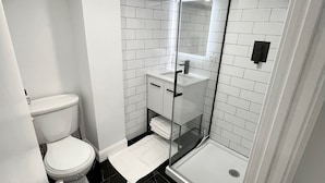 A modern bathroom with a glass-enclosed shower, white tiled walls, a white toilet, and a black tiled floor. - Modern Studio: minutes to NYC/Views, 4 miles from World Cup - MetLife Stadium (Weehawken Township)