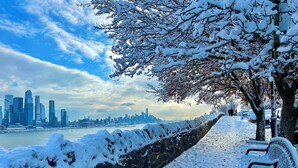 A snow-covered walkway with benches, a stone wall, and a city skyline in the background. - Modern Studio: minutes to NYC/Views, 4 miles from World Cup - MetLife Stadium (Weehawken Township)