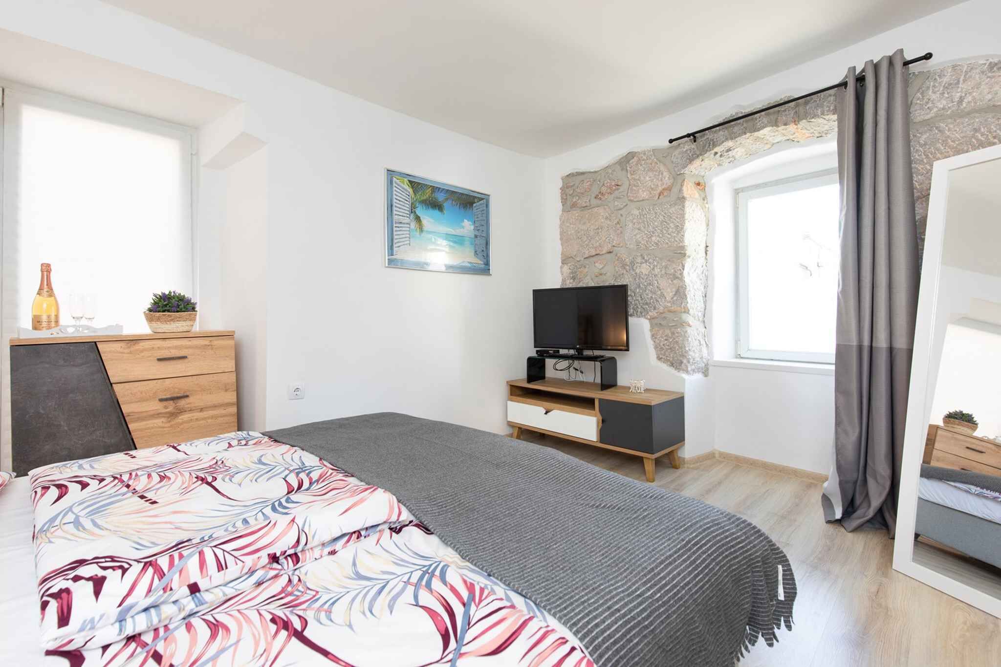 A bedroom with a bed, a TV, a dresser, a window with curtains, and a stone wall.