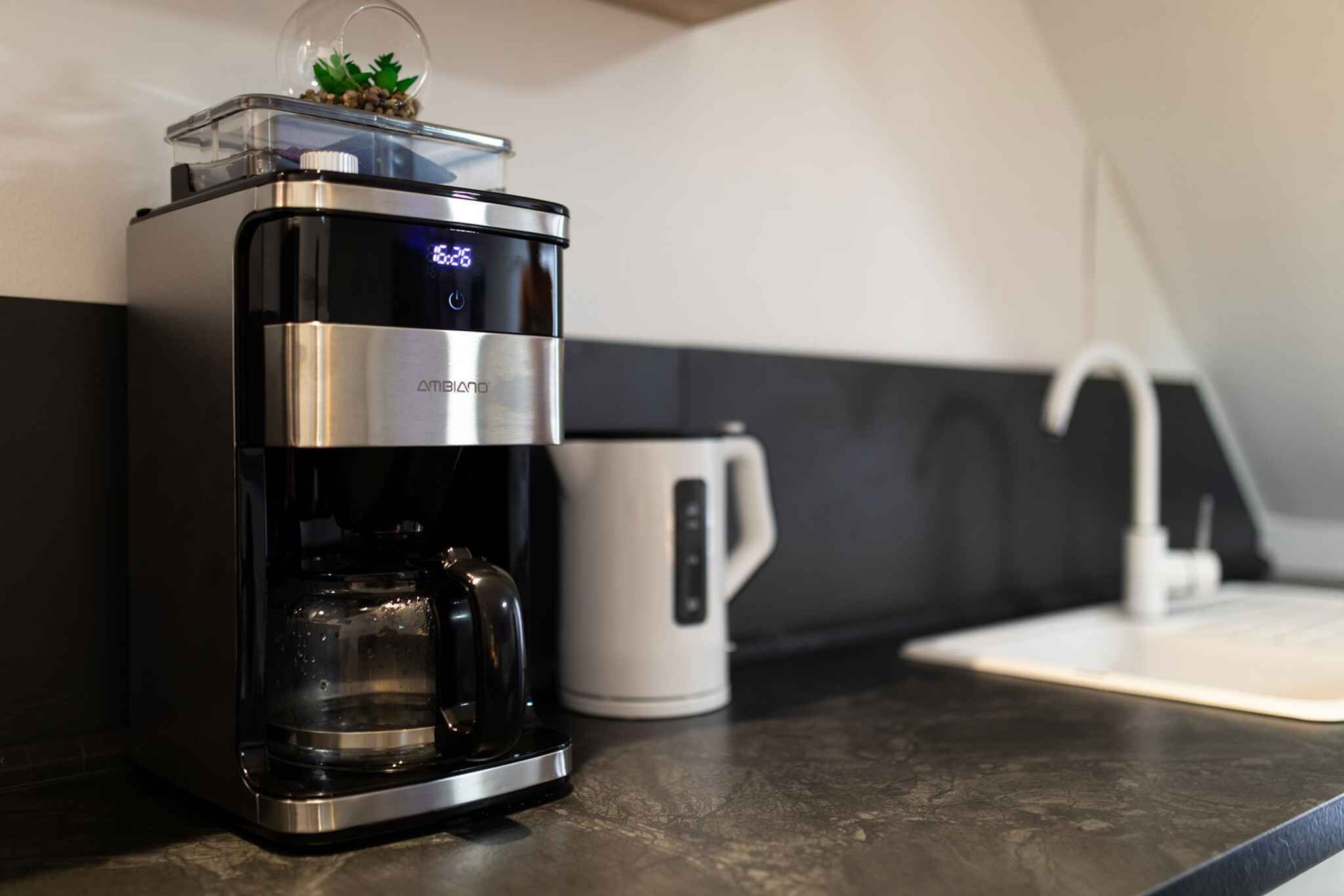 Una cafetera moderna con pantalla digital, recipiente transparente para agua y un pequeño adorno encima.