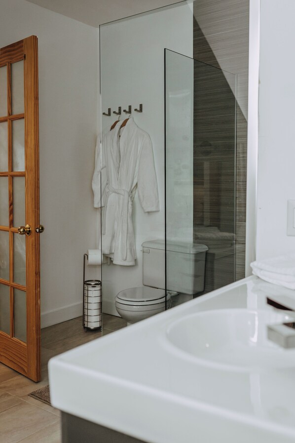 A modern bathroom with a glass shower enclosure, a wooden door, and a white bathtub. - No.5 East (Winnipeg)