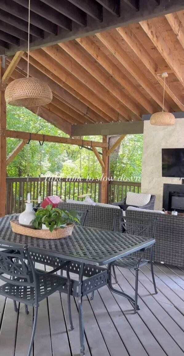 A covered outdoor seating area with a table and chairs, a hanging light fixture, and a television screen. - No.5 East (Winnipeg)