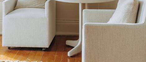 Une pièce avec un mur de couleur beige, une œuvre d’art florale encadrée, une table ronde avec une lampe et deux chaises.