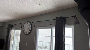 A room with a large wall clock, a window with curtains, and a view of a snowy landscape.