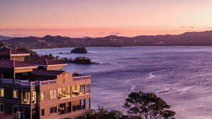 Un hotel frente al mar con varios balcones que dan al océano, una isla destacada al fondo y un paisaje montañoso.