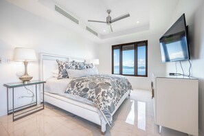 Quarto moderno com cama, mesa de cabeceira, abajur, ventilador de teto, televisão e janela com vista.