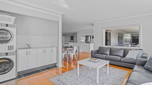 Un salon moderne avec un canapé gris, une table basse blanche et un coin cuisine doté de meubles blancs et d’un lave-linge.
