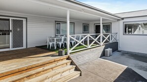 Un espace extérieur abrité, doté de rampes blanches, d’une terrasse en bois et d’un sol en béton.