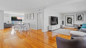 Un salon moderne avec un plancher en bois, un canapé gris, un meuble TV blanc et des œuvres d’art accrochées aux murs.
