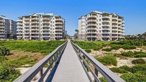 A wooden boardwalk leading to a beachfront hotel with multiple balconies and a clear sky. - Ocean Place 12 ~ Wave Watcher (Fernandina Beach)
