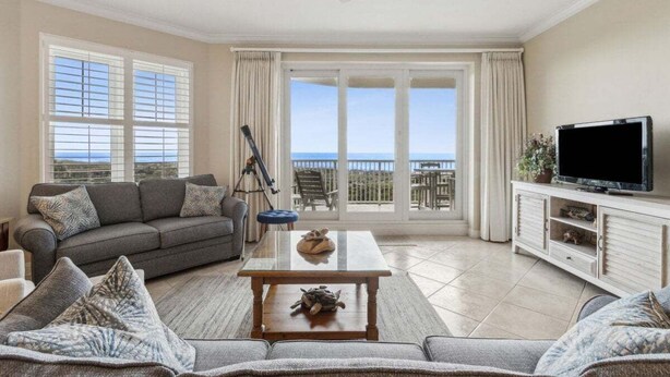 A living room with a sofa, a coffee table, a television, and a balcony with a view. - Ocean Place 12 ~ Wave Watcher (Fernandina Beach)