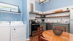 A compact kitchen with white appliances, wooden shelves, and a dining area with a patterned bowl. - Salem Boutique Downtown 3BDRM Suite (Salem)