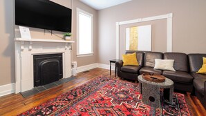 A living room with a fireplace, a black leather sofa, a patterned rug, and a flat-screen TV mounted above the fireplace. - Salem Boutique Downtown 3BDRM Suite (Salem)