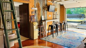 A rustic interior with wooden walls, a water dispenser, a TV, and a bar area with stools. - Tiny cabin/guest house with hot tub and pool surrounded by nature (Lakehills)