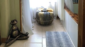 A narrow hallway with a wooden floor, a decorative fish on the wall, a frog statue, a woven basket with cushions, and a window with sheer curtains. - Tiny cabin/guest house with hot tub and pool surrounded by nature (Lakehills)