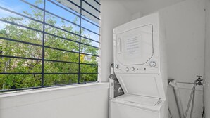 A laundry room with a window, a washing machine, and a hose.