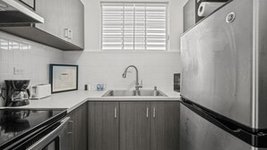 A compact kitchen with a stainless steel refrigerator, a double sink, and a coffee maker.