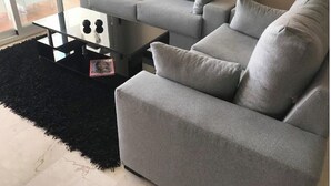 En grå sofa med et sofabord i glas og en sort måtte.