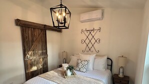 Un dormitorio con estructura de cama de madera, una lámpara colgante, aire acondicionado instalado en la pared y un adorno mural.