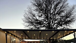 Un espacio al aire libre cubierto con suelo de grava, un edificio de madera con una ventana y un árbol al fondo.