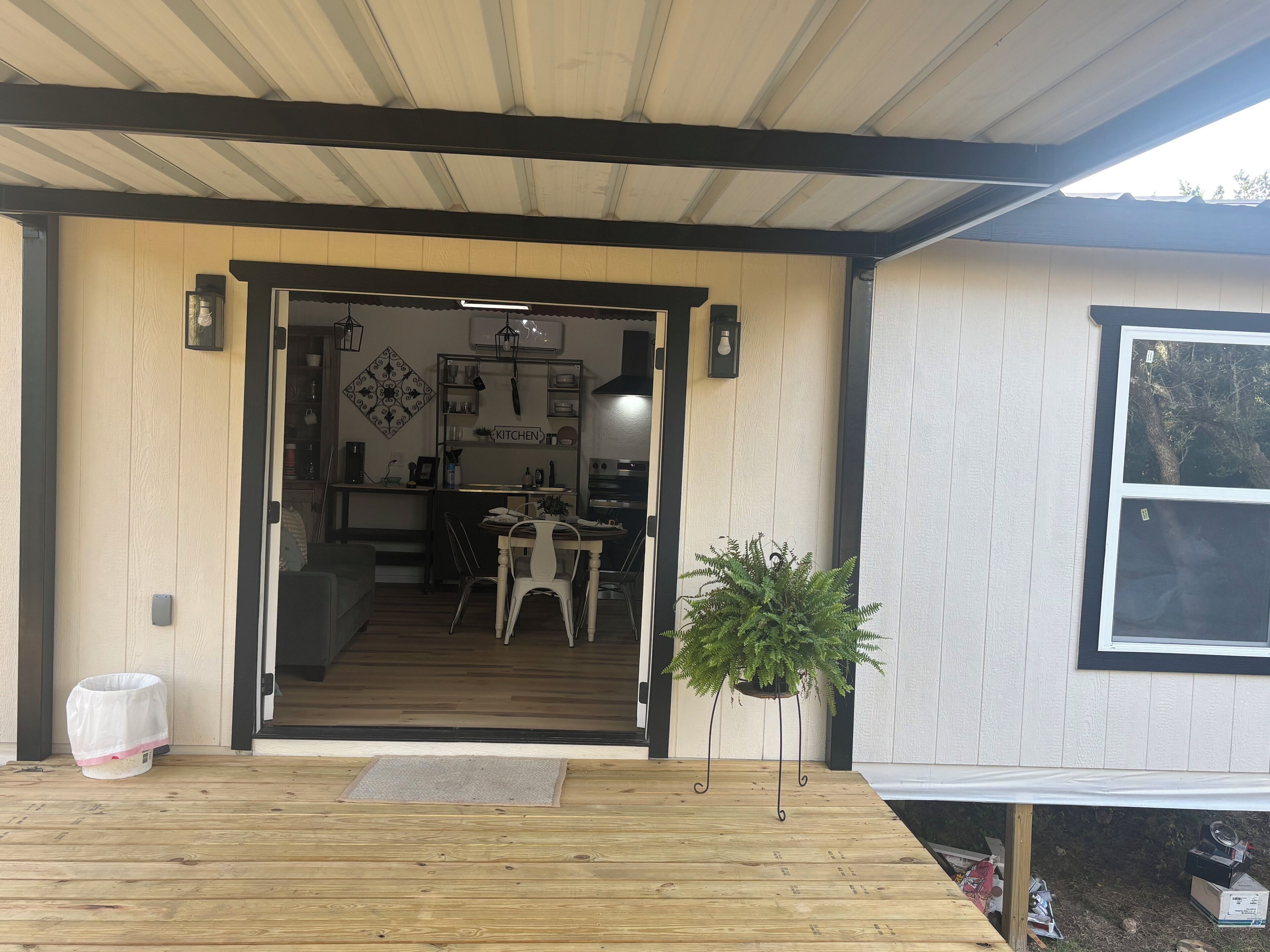A wooden deck with a bench, a potted plant, and a door leading to a kitchen area with a dining table and chairs.