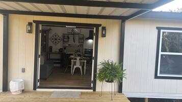 A wooden deck with a bench, a potted plant, and a door leading to a kitchen area with a dining table and chairs.