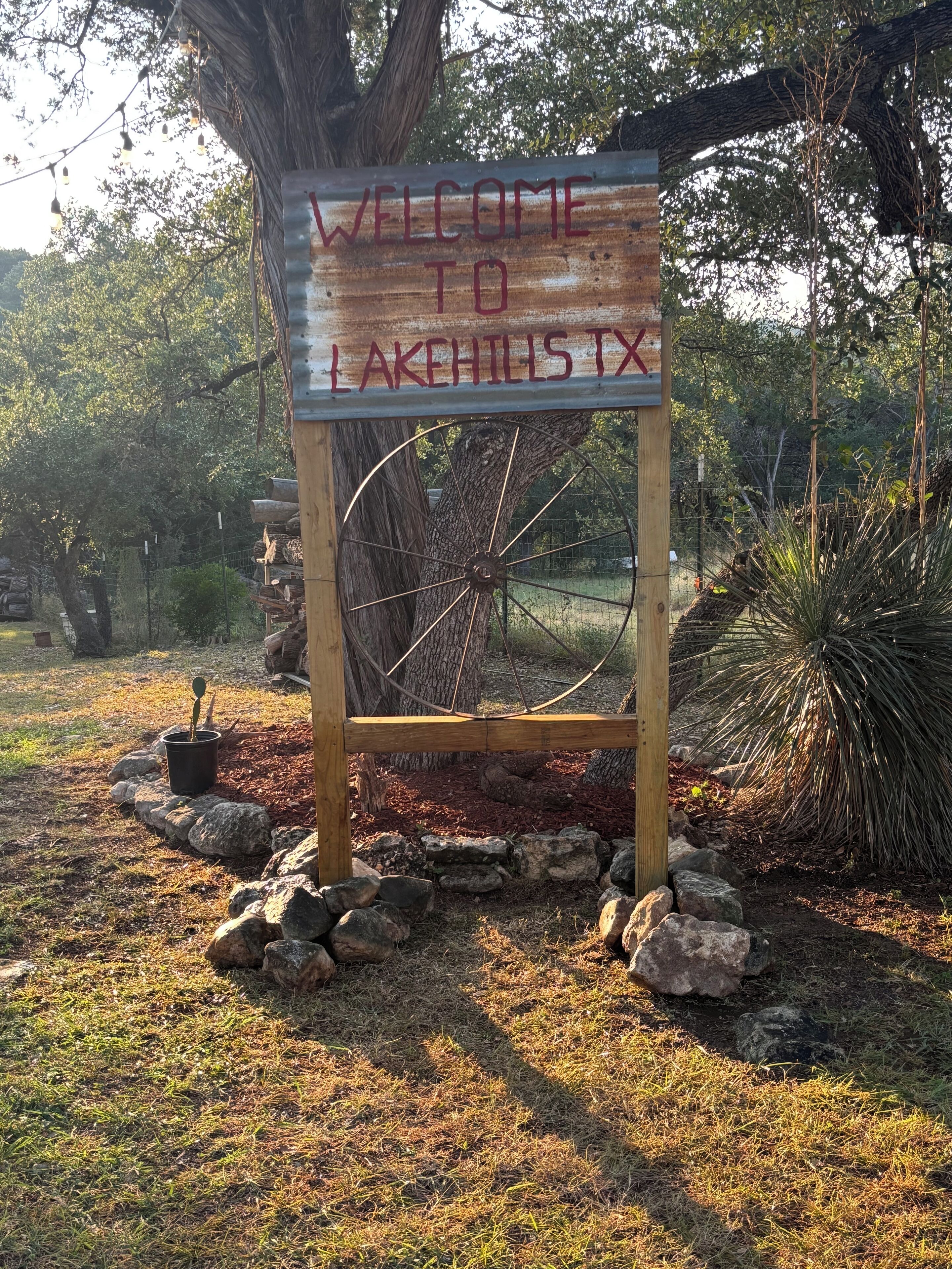 Un panneau en bois sur lequel est écrit « BIENVENUE À LAKEHILLS, TEXAS », entouré de rochers et de plantes.