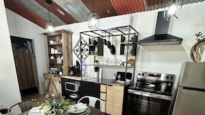 Una cocina moderna con electrodomésticos de acero inoxidable, una mesa de comedor de madera dispuesta para cuatro comensales y un techo rústico.