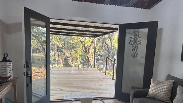 Una puerta abierta que da a una terraza de madera con mobiliario exterior, un sofá y un adorno de pared.