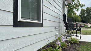 A house with white siding, a window with a black frame, and a black outdoor chair. - The Relaxing House - Quiet 2 Bedroom Home (Raymond)
