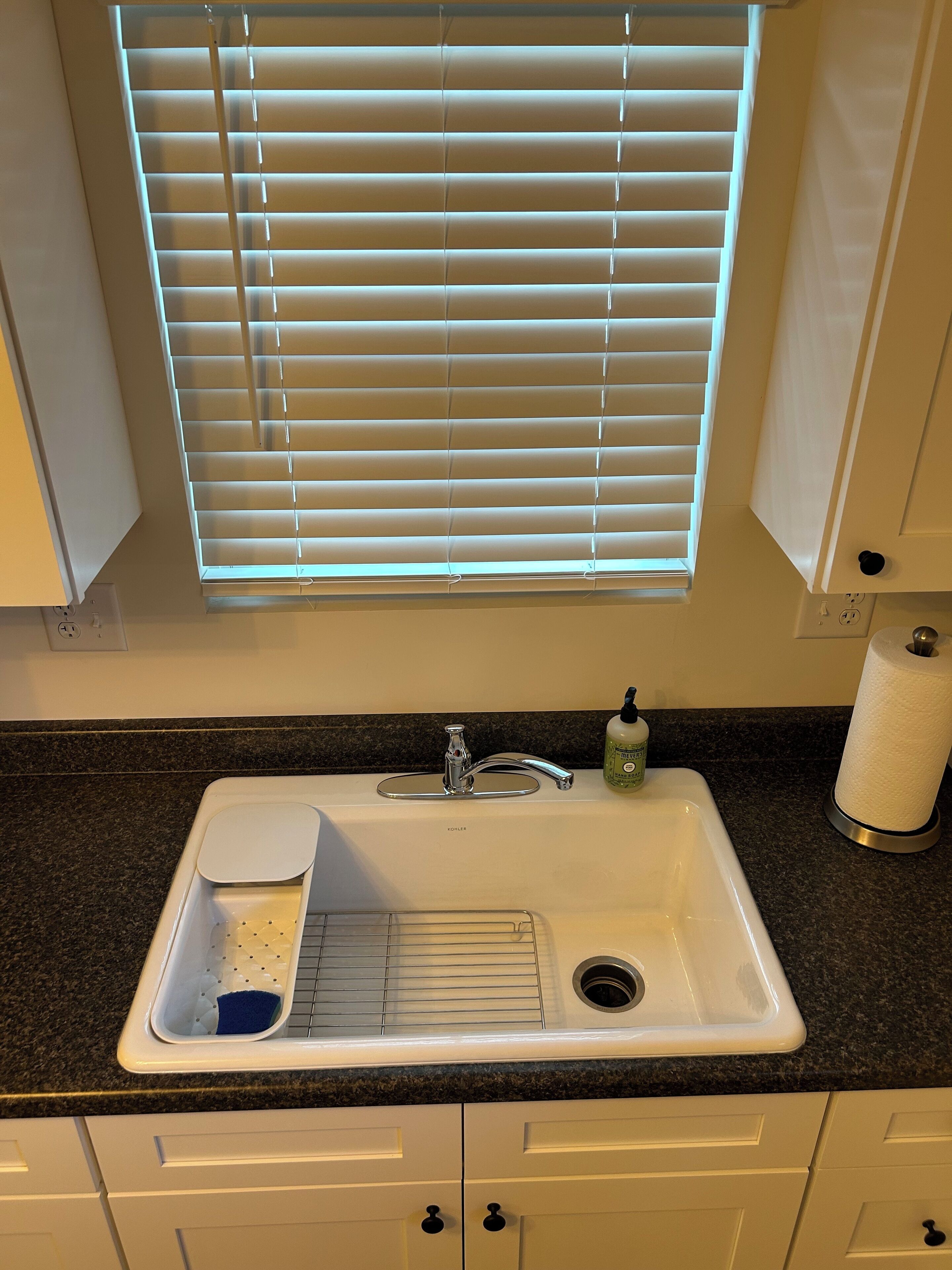A kitchen with a white sink, a faucet, a soap dispenser, and a paper towel holder.