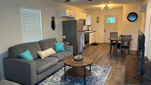 A compact living space with a sofa, a coffee table, a dining table with chairs, a kitchen area with cabinets and appliances, and a ceiling fan. - The Relaxing House - Quiet 2 Bedroom Home (Raymond)