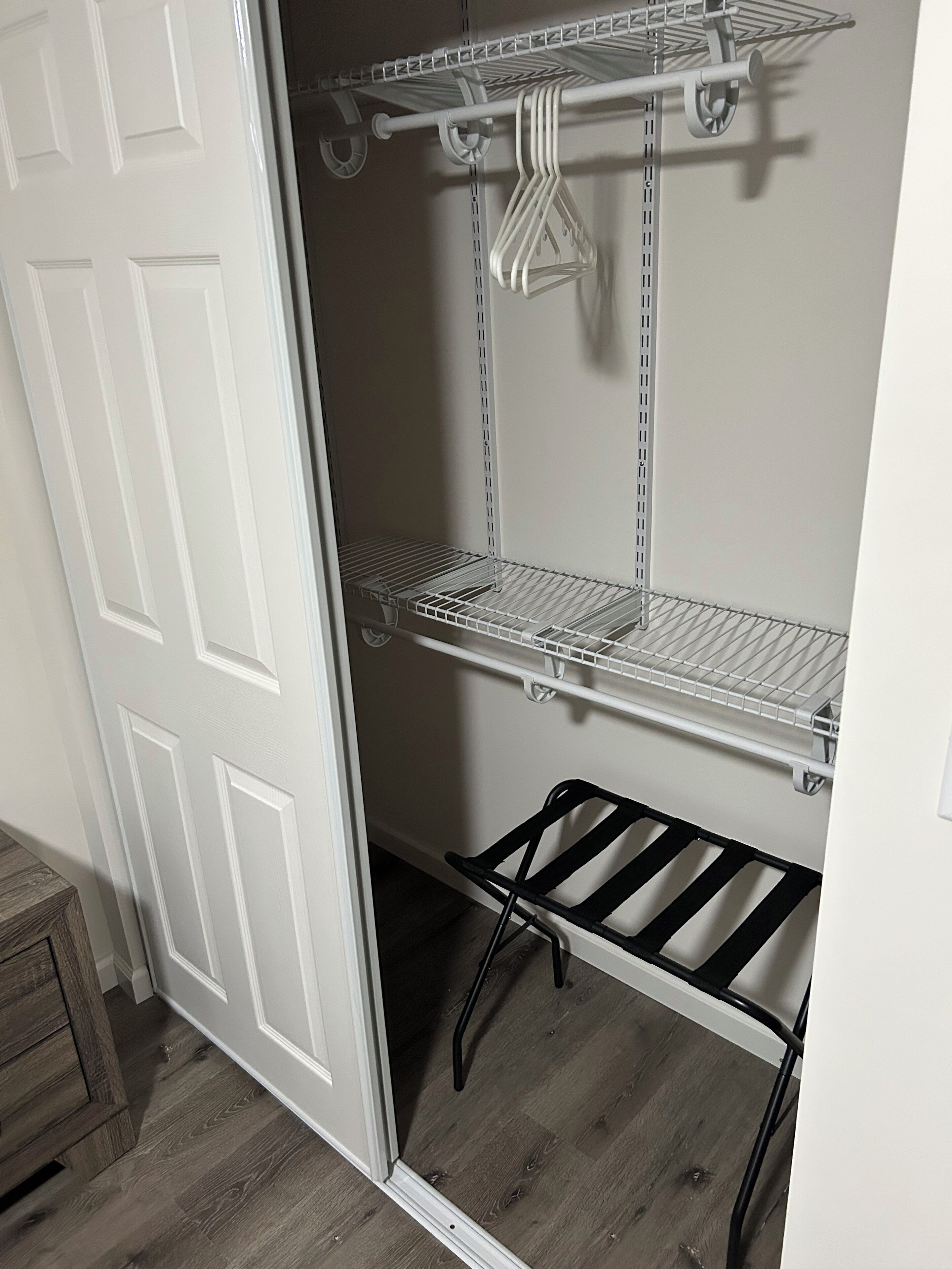 A closet with white doors, metal shelves, and a black rack.