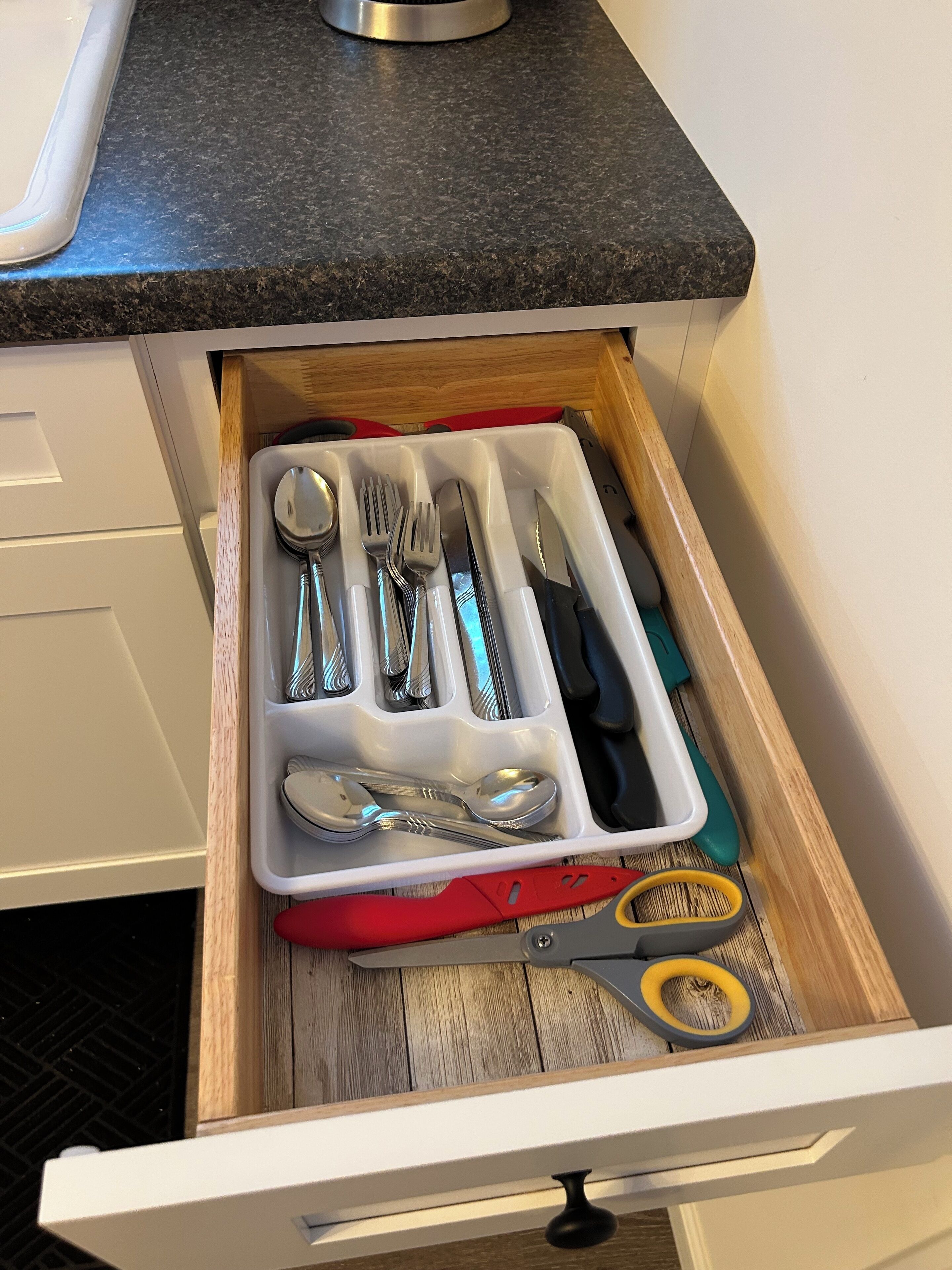 A kitchen drawer with utensils and a cutting board.