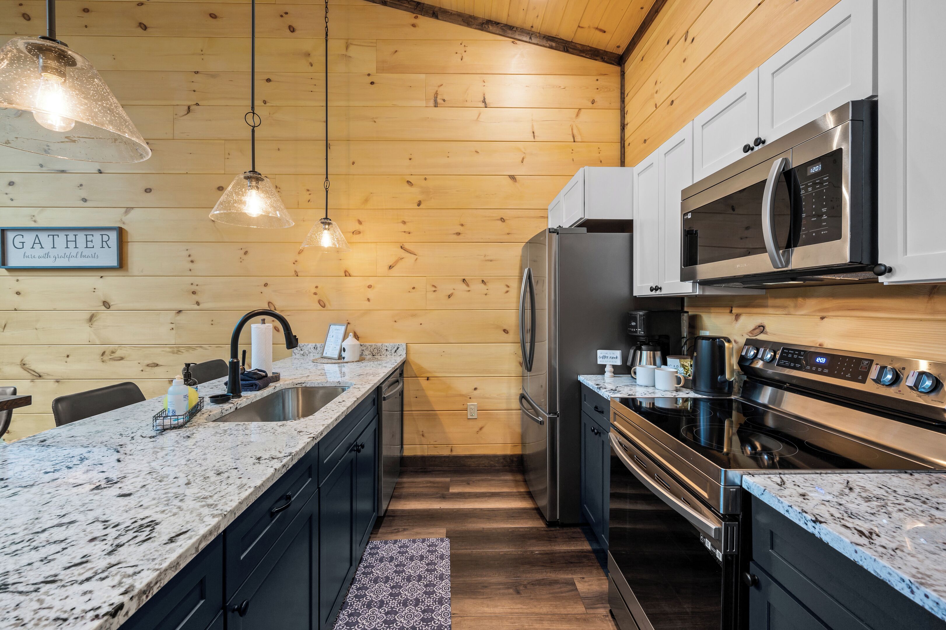 A kitchen with wooden walls, granite countertops, stainless steel appliances, and pendant lighting.
