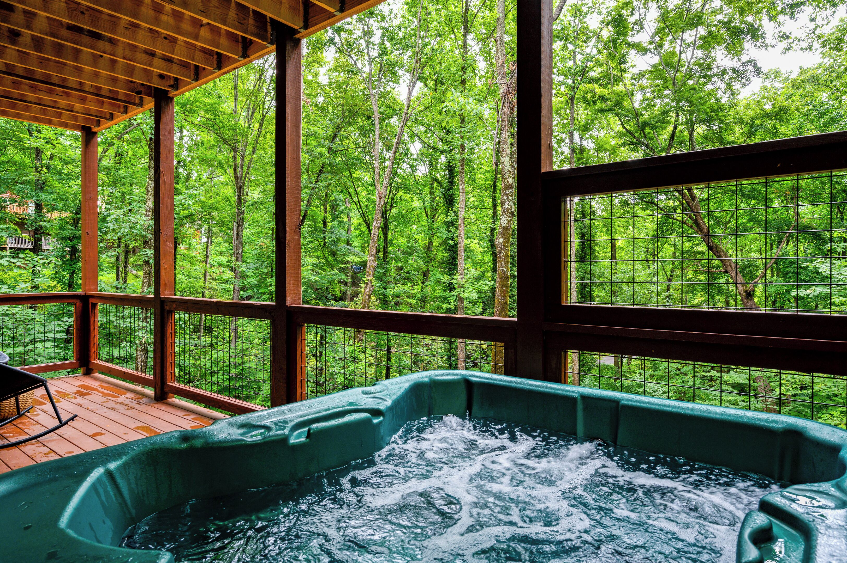 A hot tub with a view of a forest through large windows.
