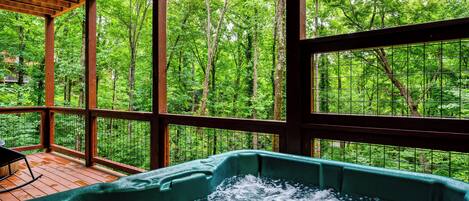 A hot tub with a view of a forest through large windows.