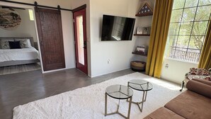 Una sala de estar moderna con un sofá marrón, dos mesas de vidrio, un televisor grande y una puerta corrediza que da a otra habitación.