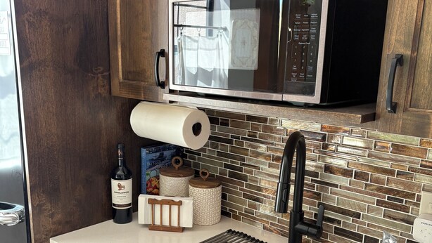 Una cocina con armarios de madera, un lavamanos de acero inoxidable, un microondas y un rollo de toallas de papel.