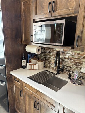 A kitchen with wooden cabinets, a stainless steel sink, a microwave, and a roll of paper towels. - Charming 1-bdrm/1-bath casita. Located in beautiful Cobo Catalina neighborhood. (Tucson)