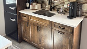 Una cocina con armarios de madera, un refrigerador de acero inoxidable, un microondas, un fregadero y una cafetera.