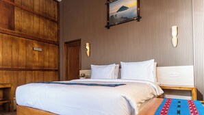 Una habitación de hotel con piso de madera, una cama con ropa blanca, una mesita de noche y un aplique de pared.