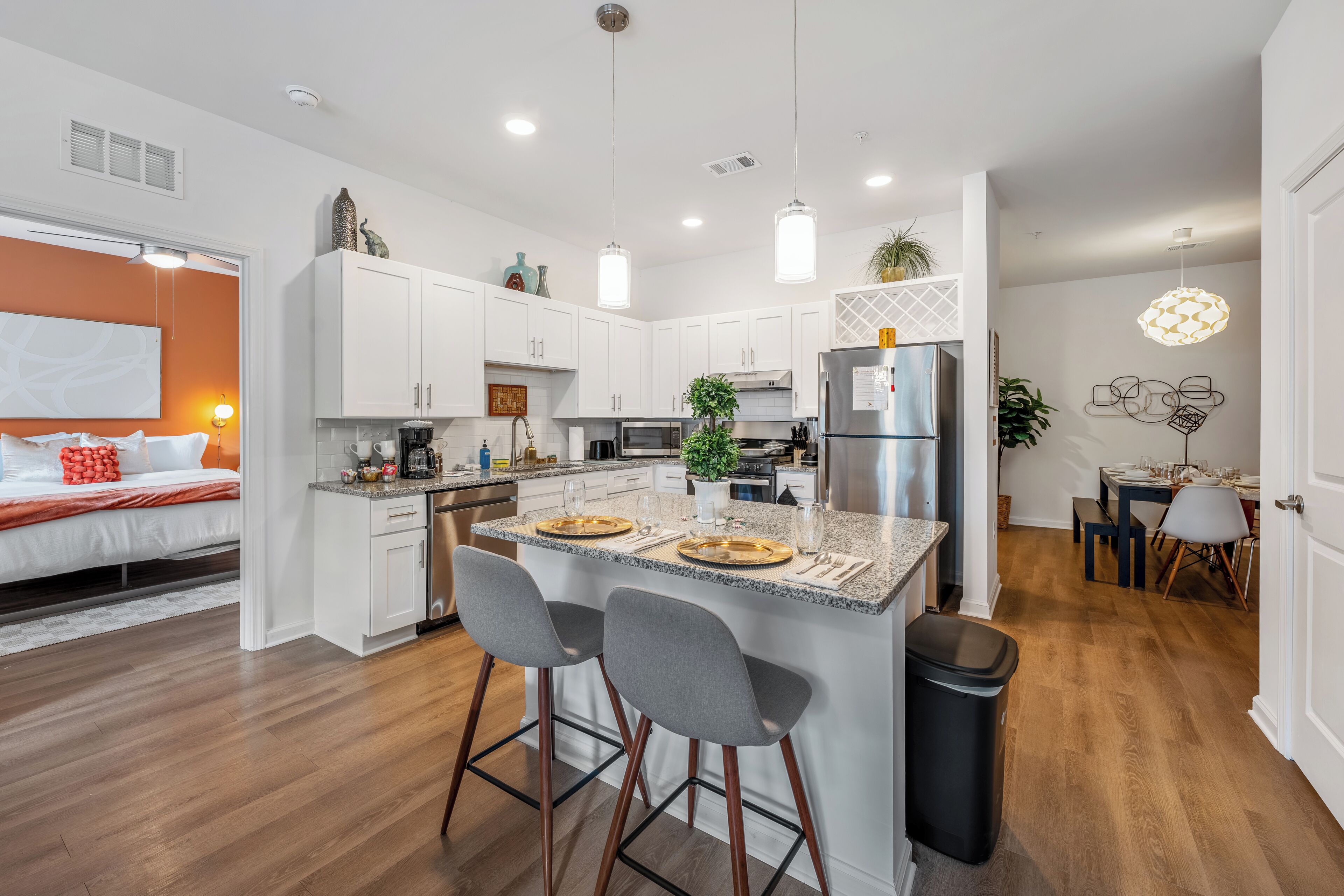 A modern kitchen with white cabinets, a central island with bar stools, stainless steel appliances, and pendant lighting.